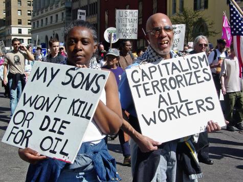 Two people hold up signs at an anti-war protest organized by ANSWER Coalition, demonstrating against the Iraq War. The signs read 'My sons wont kill or die for oil' and 'Capitalism terrorizes all workers.'