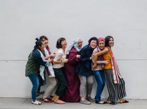 7 laughing women from different backgrounds stand together 