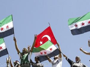 Syrian refugees wave Turkish and Syrian Independence flags during a protest against Assad at Yayladagi refugee camp