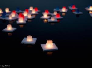 Multiple white, red, and blue candles sit on a white square base float on dark still water