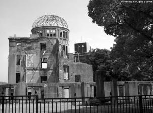 Black and white abandoned building with a smashed dome roof and no windows behind a black metal fence