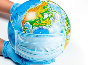 Two hands wearing blue latex surgical gloves hold a globe of the Earth wearing a blue surgical mask