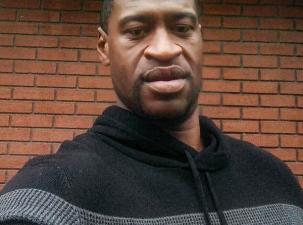 African American man wearing a black and grey sweater takes a selfie infront of a brick wall