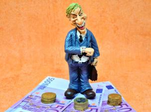 Cartoon-like figurine of a greedy smiling white man in a suit standing on top of Euro notes and piles of coins