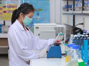 Asian woman works in a laboratory wearing a mask and a white lab coat