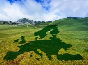 A green silhouette map of Europe lies on top of a mountain landscape