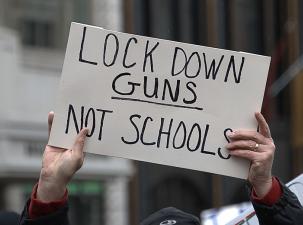 Hands hold up a white cardboard sign saying lock down guns not schools
