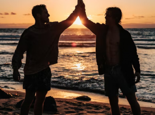 Silhouette's of two happy men on the beach at sunset high-fiving over the sun