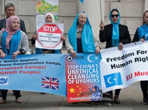 5 serious women stand holding a banner supporting the rights fo the Uyghur people