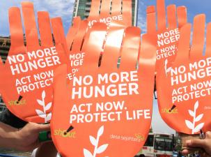 6 giant orange hands are held in the air display the words 'No more hunger. Act now'