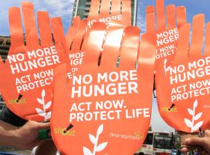 Six giant orange hands are held in the air display the words 'No more hunger. Act now'