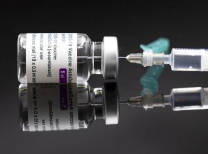 Image of a AstraZeneca COVID-19 vaccine vial on its side with a needle in the top
