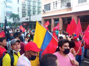 Protesters march down a street in Ecuador against rising food prices and inflation. Many protesters carry flags.