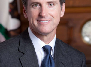 Image of California Governor Gavin Newsom, a white man wearing a black suit smils into the camera 