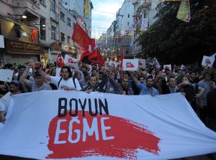 Protesters at Gezi Park in Istanbul Turkey hold a larg white banner which says 'Boyun Egme'. They are holding banners and waving flags.