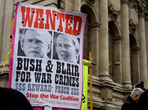 A wanted poster is hung infront of a government building in London. Pictures of Tony Blair and George Bush sit under a red 'Wanted' banner with the words 'Bush and Blair for war crimes' written in black underneath