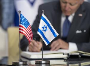 Image of Israeli and US flags with President Joe Biden signing document in background.