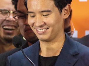 Pita Limjaroenrat, leader of the Future Forward Party. A Thai man wearing a blue suit and black tshirt smiles whilst looking down to the microphone 