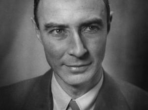 Black and white portrait photograph of J. Robert Oppenheimer &ndash; Father of the Atomic Bomb. A middle aged gentleman wtih dark hair wears a suit and looks away from the camera