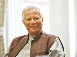 Bangladeshi Nobel Peace Prize winner Muhammad Yunus smiles at the camera. He is wearing a grey shirt and brown waistcoat