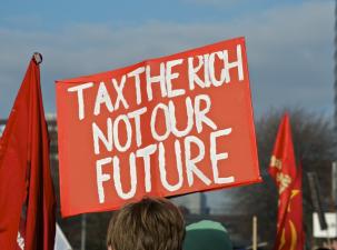 A protester holds a large orange sign which says 'Tax the rich not our future'