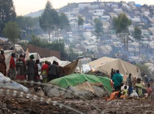 A refugee camp full of Congolese refugees. There are many tents in an area which is surrounded by barbed wire. The camp sprawls across the mountains.