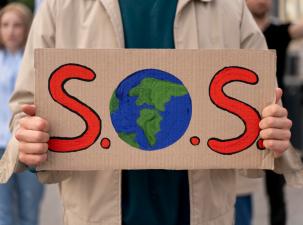 woman holding a sign with the letters SOS while protesting global warming