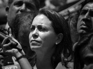 Black and white image of Venezuelan politician Mar&iacute;a Corina Machado. She looks seriously off to one side standing in a crowd of people.