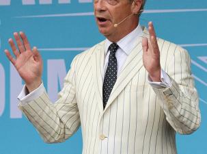 Nigel Farage wearing a white pinstripe suit addresses a Reform UK rally at Trago Mills, Devon