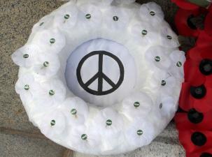 White peace poppies made into a wreath sit on the floor next to a red wreath for Remembrance Day in the UK.