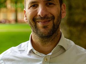 Head shot photo of Green Party London Assembly Member Zack Polanski taken outside in a green park.