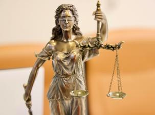 A golden staue of the Lady Scales of Justice. Blindfolded she holds high the scales which are evenly balanced, in the other hand she holds a sword.