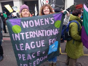 Two women smiling while holding a large banner that reads, "Women's International League for Peace & Freedom," at a demonstration.