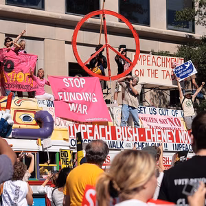 Colourful image of a bus decorated with peace symbols there are protesters riding on top displaying anti-war signs and against funding the war