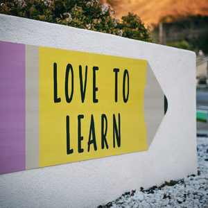 A big white concrete sign displays a graphic of a large yellow pencil with the words 'love to learn' on it