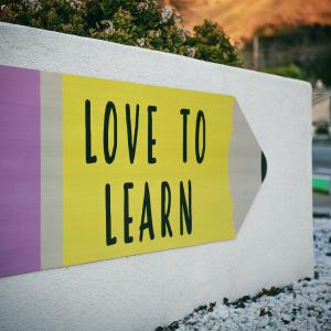 A big white concrete sign displays a graphic of a large yellow pencil with the words 'love to learn' on it