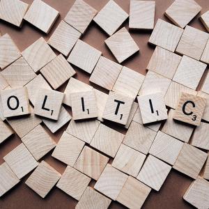 Beige coloured wooden Scrabble letters spell out the word politics on top of many other blank square pieces