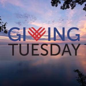 A serene sunset over a calm lake with the text "GIVING TUESDAY" prominently displayed in front.