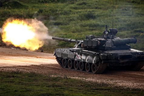 A black army tank is driving along a dirt road firing into the road
