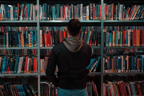 Causally dressed man with his back to the camera is looking through books on a bookshelf in a library