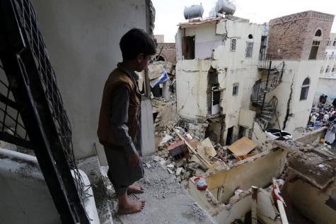 A sad child stands on the edge of a destroyed building overlooking the debris and destruction below