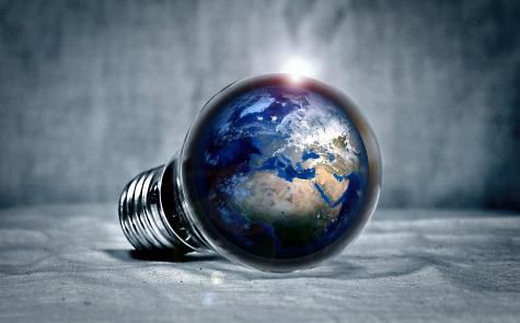 The planet Earth sits inside a light bulb resting on its side. The bulb sits in an empty grey space