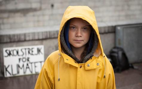 Determined young girl stands in the rain wearing a yellow rain jacket with the hood up
