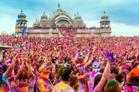  2014 Festival of Colors in Texas, large crowd covered in pink powder celebrate infront of a temple