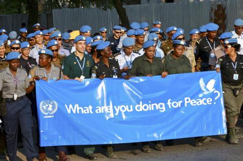 United Nations peacekeepers stand in their uniforms and blue hats holding a giant blue banner that says 'What are you doing for peace?'