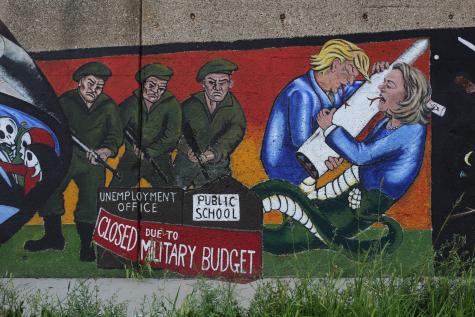 Mural on a wall of politicians and soldiers hugging weapons infront of a school and unemployment office which are now closed