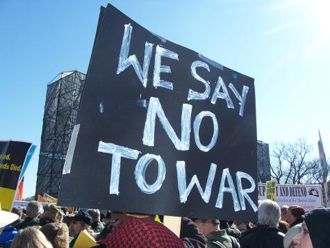 At an anti-war demonstration there is a large black sign that says 'We Say No To War'.