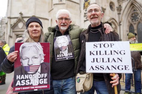 Three people, two men, one women, stand infront of the London High Court in support of Julian Assange. They hold signs against his extradition to the U.S. and in support of press freedom. 