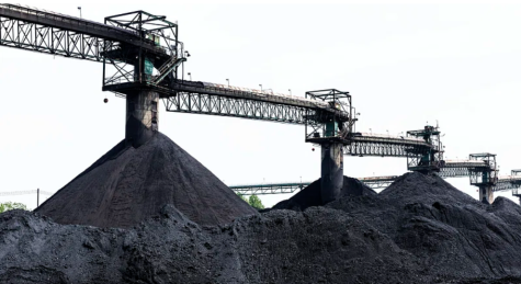 Four huge piles of black coal sit under machniery for processing at a coal mine