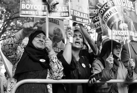 Black and white image of many female protesters behind a barrier holding signs fighting for the boycott of Israel